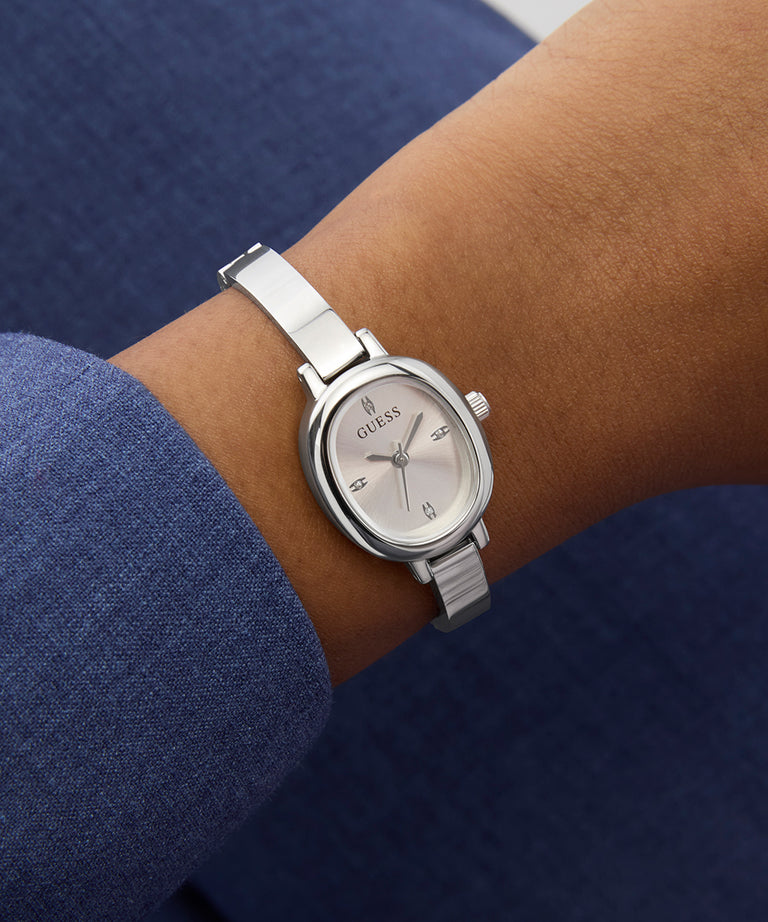 Silver Guess watch on a wrist with a blue sleeve against a dark background