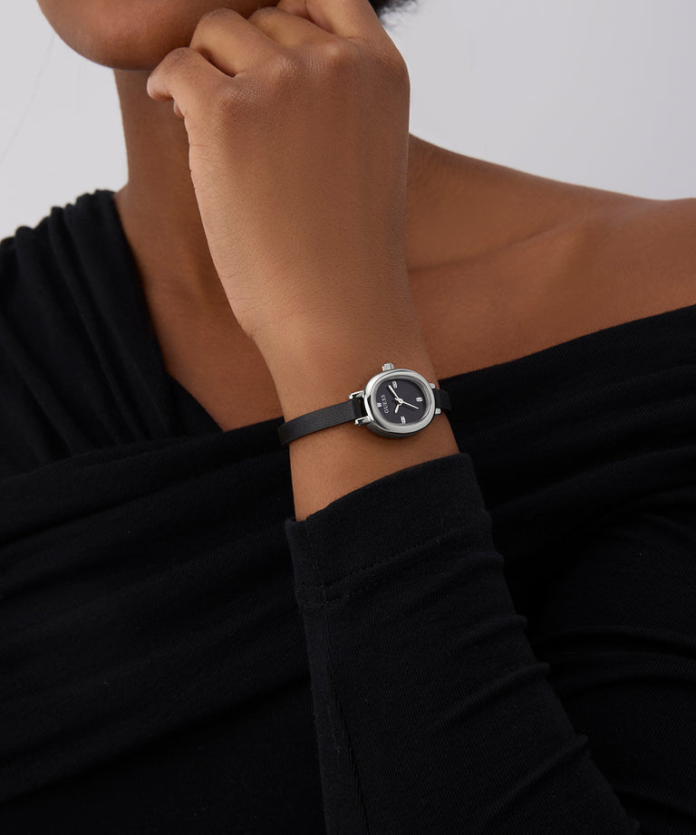 Person wearing a black GUESS Ladies Black Silver Tone Analog Watch with a white face on a plain background