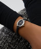 Black GUESS Ladies Black Silver Tone Analog Watch on a person's wrist with a blurred background