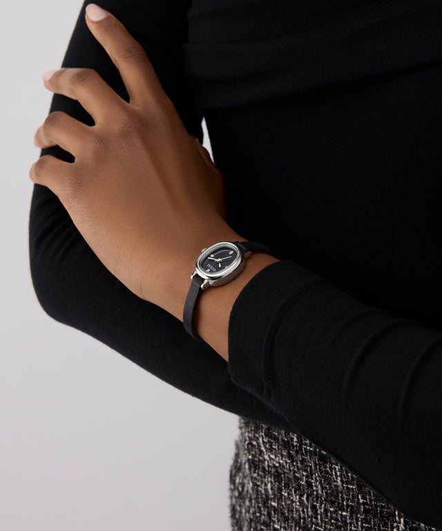 Person wearing a black GUESS Ladies Black Silver Tone Analog Watch on a plain background