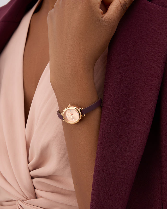 GUESS Ladies Red Rose Gold Tone Analog Watch on a wrist with a blurred background