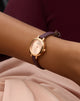 GUESS Ladies Red Rose Gold Tone Analog Watch with a purple strap on a wrist against a blurred background