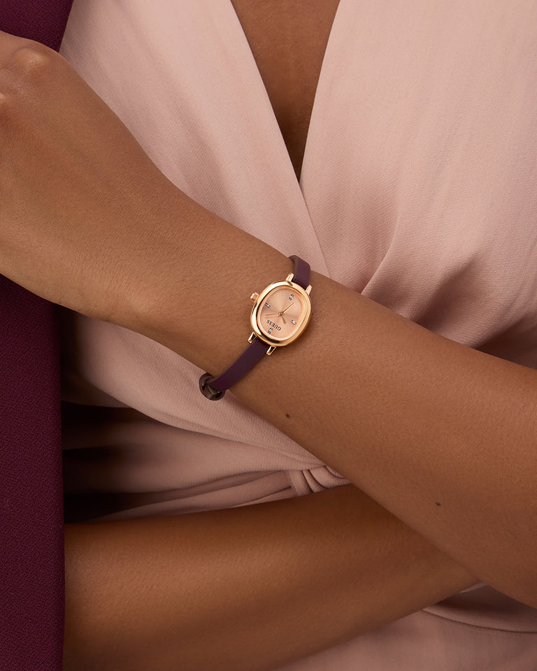 Gold GUESS Ladies Red Rose Gold Tone Analog Watch with a purple strap on a wrist against a soft pink fabric background