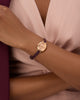 Gold GUESS Ladies Red Rose Gold Tone Analog Watch with a purple strap on a wrist against a soft pink fabric background