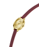 A GUESS women's watch featuring an oval gold-tone case, a champagne dial with crystal hour markers, and a burgundy leather strap, shown on a plain white background. lifestyle