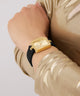 Gold watch on a wrist with a gold sleeve against a light gray background GW0926L2