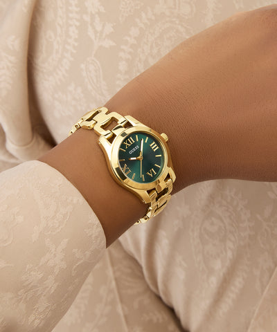 Gold GUESS Ladies Gold Tone Analog Watch with a green face on a wrist against a neutral background