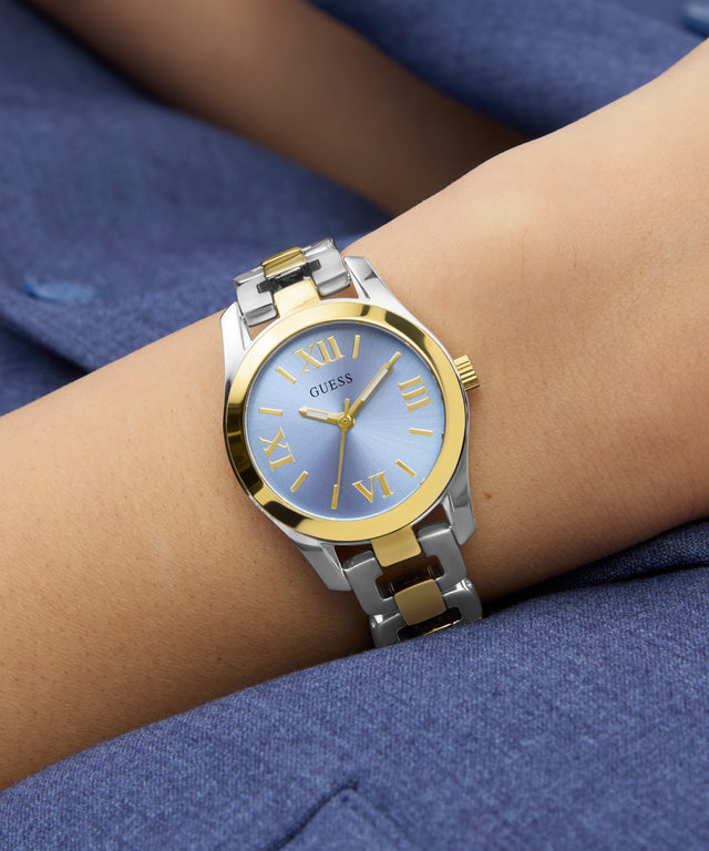GUESS Ladies 2-Tone Analog Watch with gold and silver band on a wrist against a blue background