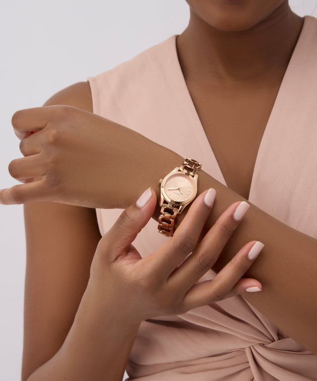 Woman wearing a GUESS Ladies Rose Gold Tone Analog Watch on a plain background