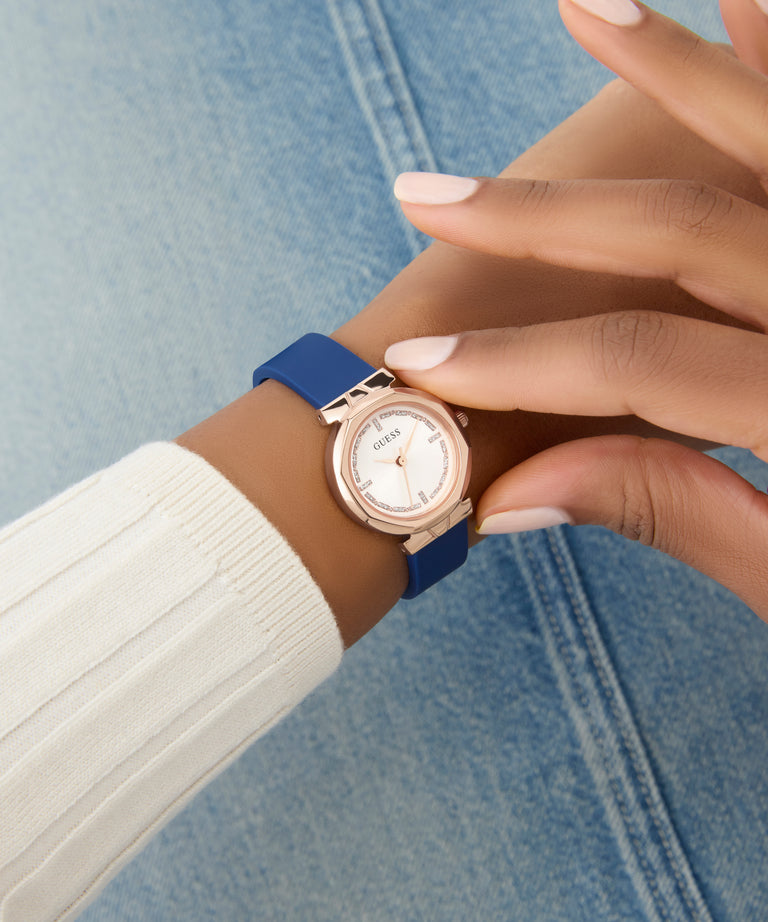 Wrist wearing a GUESS Ladies Blue Rose Gold Tone Analog Watch with a blue strap against a denim background
