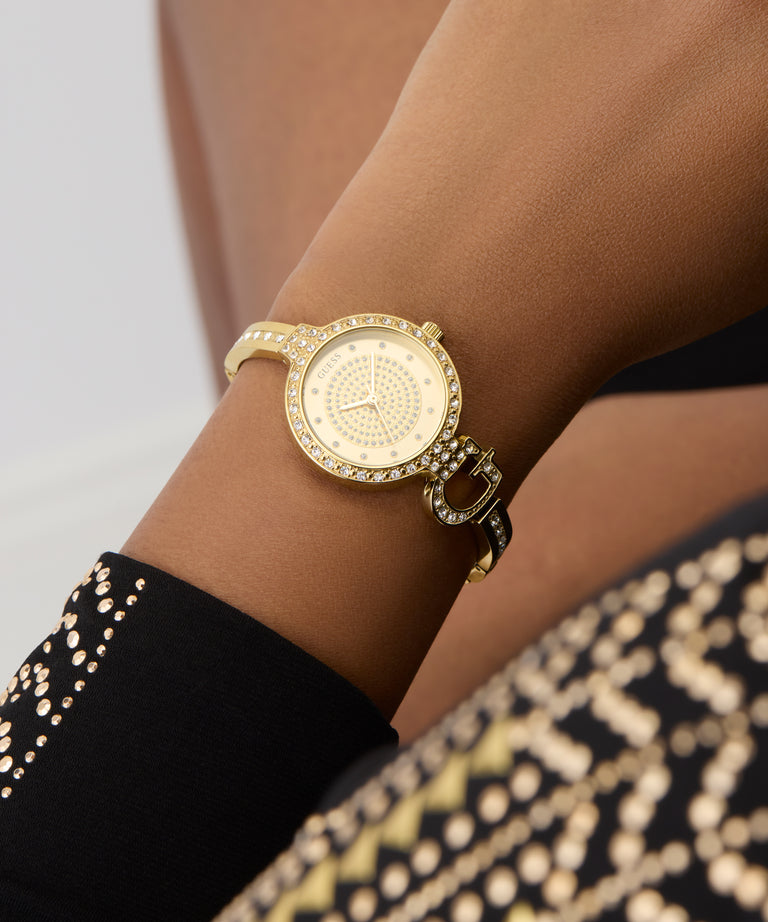 GUESS Ladies Gold Tone Analog Watch on a wrist with a blurred background