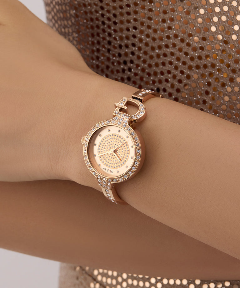 GUESS Ladies Rose Gold Tone Analog Watch with diamond accents on a wrist against a patterned background