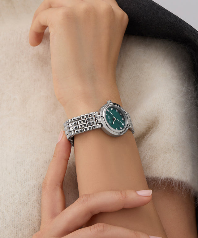Close-up of a wrist wearing a silver watch with a green face on a soft background