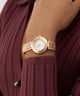 GUESS Ladies Rose Gold Tone Analog Watch on a wrist with a maroon background