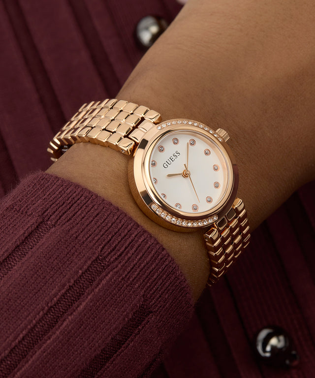 GUESS Ladies Rose Gold Tone Analog Watch with a white face on a wrist against a maroon background