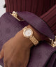 GUESS Ladies Rose Gold Tone Analog Watch on a wrist with a purple textured handbag