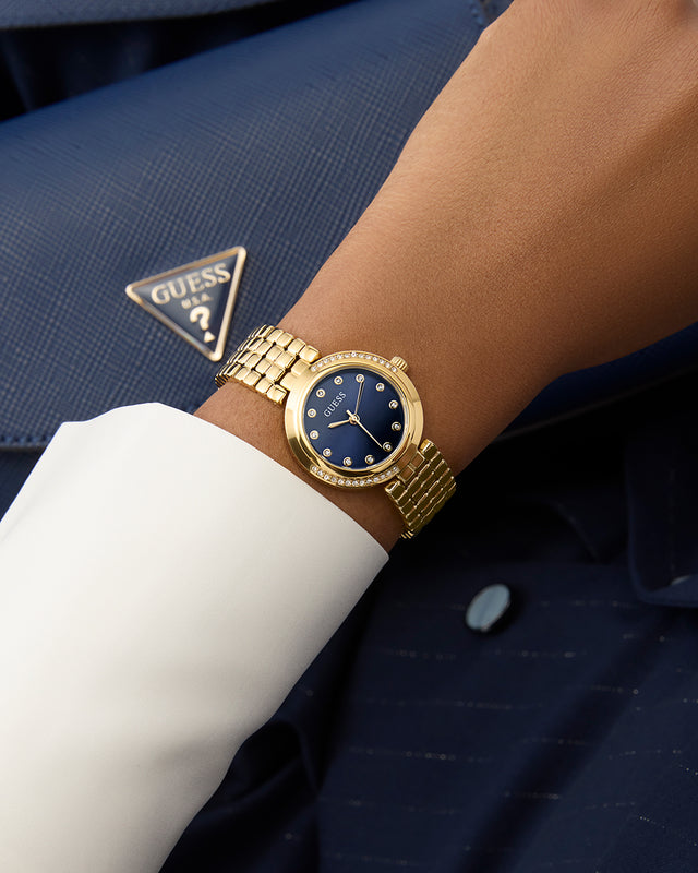 Gold watch on a wrist with a blue dress shirt and navy suit jacket, featuring a Guess logo. GW0930L4