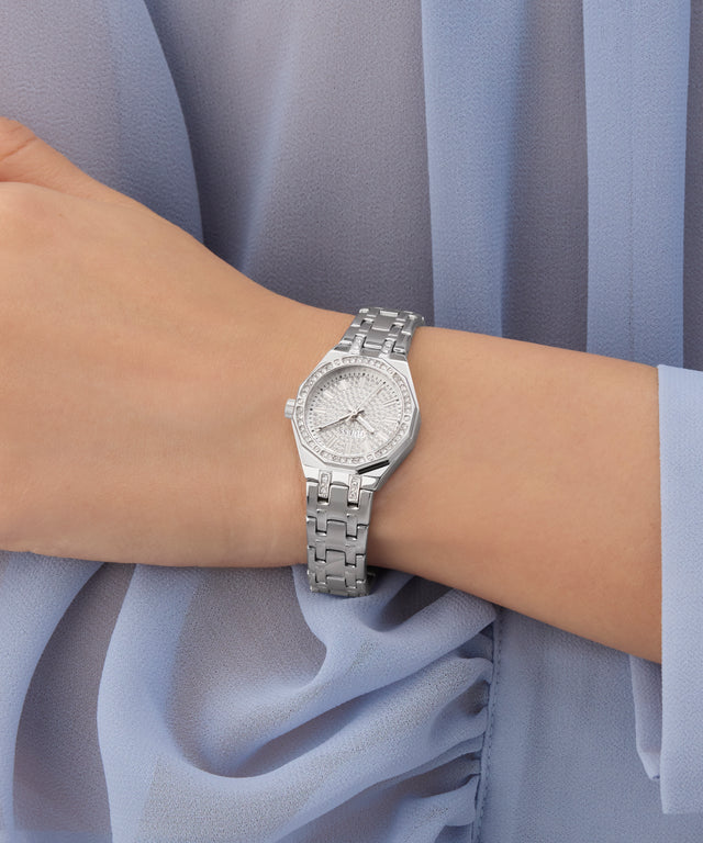 Silver GUESS Ladies Silver Tone Analog Watch on a wrist with a light blue fabric background