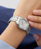 Silver GUESS Ladies Silver Tone Analog Watch with diamond accents on a wrist against a blue background