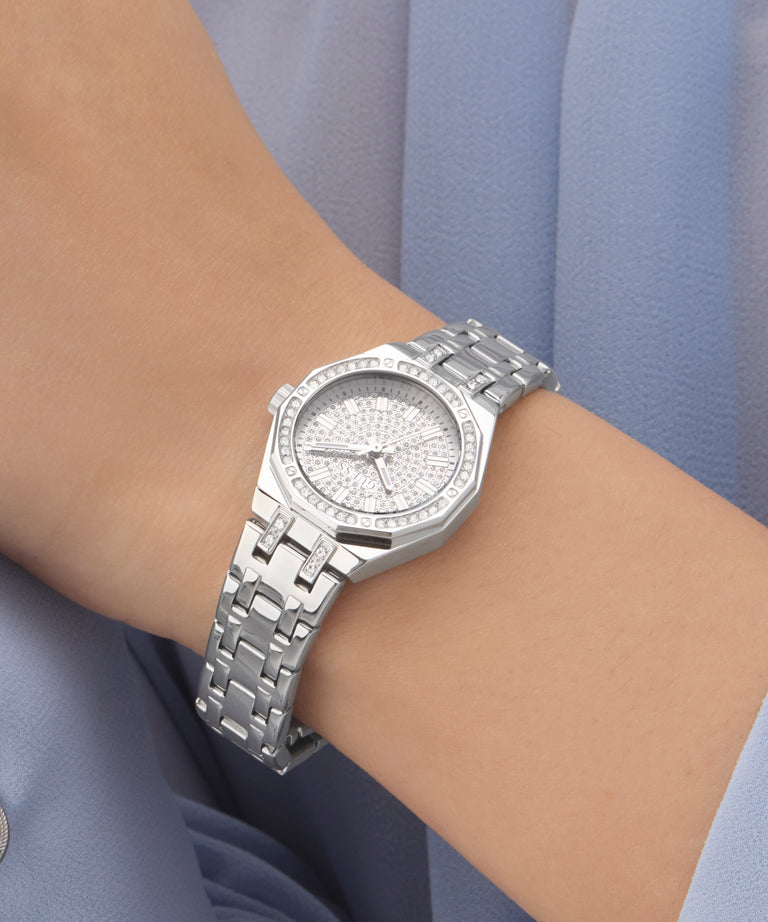 Silver GUESS Ladies Silver Tone Analog Watch with diamond accents on a wrist against a light blue background