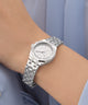 Silver GUESS Ladies Silver Tone Analog Watch with diamond accents on a wrist against a light blue background