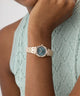 Rose gold watch with green face on a wrist against a light green textured background