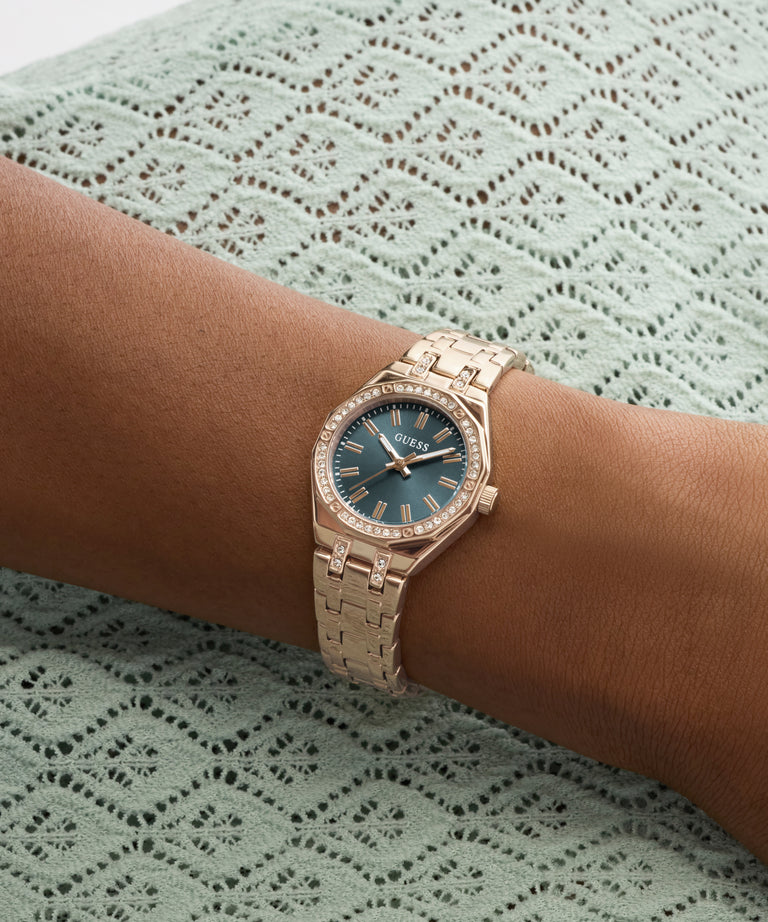 Rose gold watch with a blue face on a wrist against a green lace background