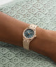 Rose gold watch with a blue face on a wrist against a green lace background