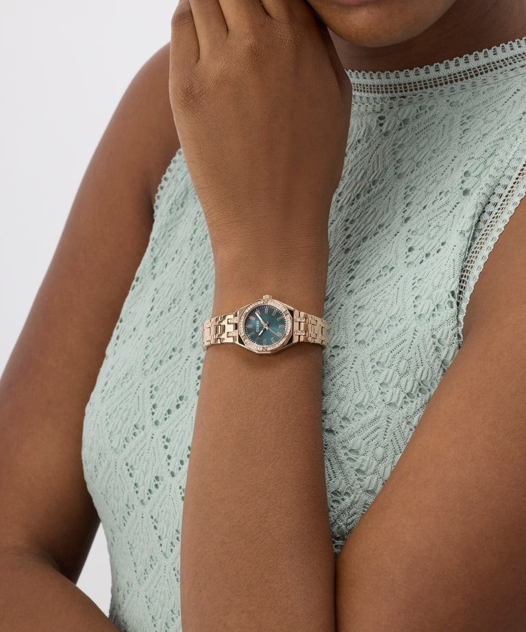 Woman wearing a rose gold watch with a blue face on a plain background