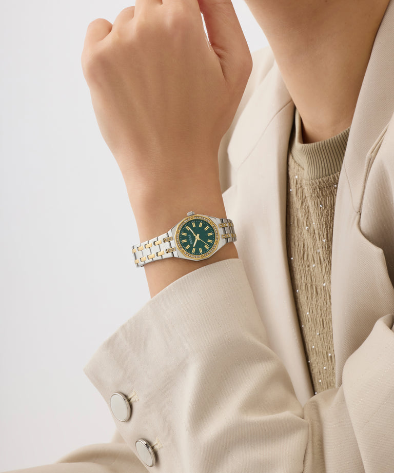 Close-up of a person wearing a silver watch with a green face on a light background