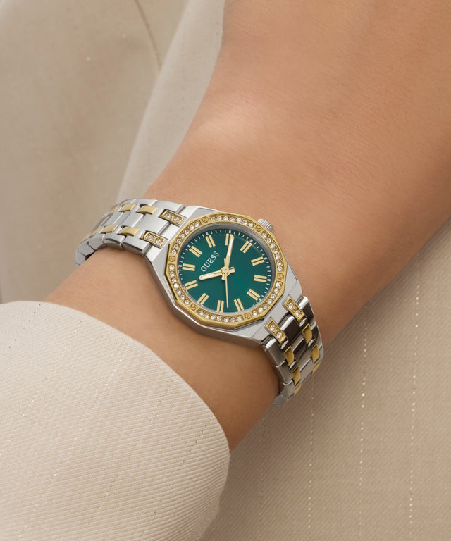Silver and gold watch with a green face on a wrist against a beige background