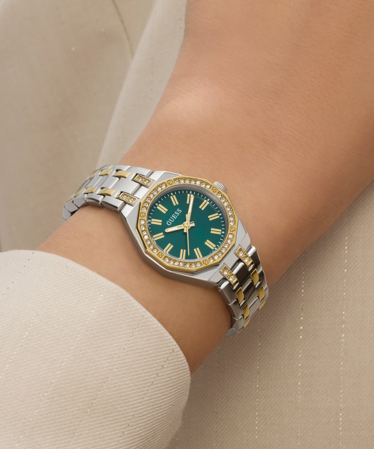 Silver and gold watch with a green face on a wrist against a beige background