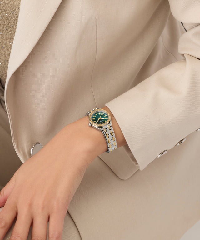 Close-up of a wrist wearing a watch with a detailed face, set against a neutral background.