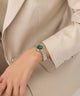 Close-up of a wrist wearing a watch with a detailed face, set against a neutral background.