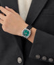 Person wearing a GUESS Ladies Black Silver Tone Analog Watch with a green face on a black suit background