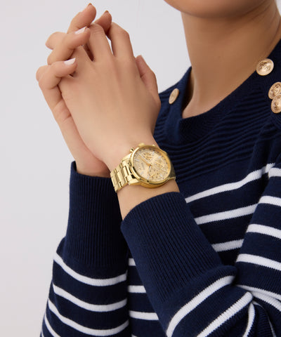 Gold GUESS Ladies Gold Tone Multi-function Watch on a wrist with a navy and white striped sweater