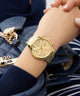 Gold GUESS Ladies Gold Tone Multi-function Watch on a person's wrist with a blue textured bag in the background