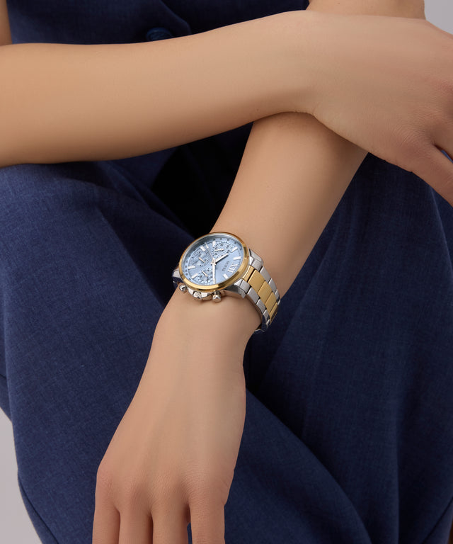 GUESS Ladies 2-Tone Multi-function Watch on a person's wrist with a dark blue fabric background