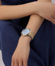 GUESS Ladies 2-Tone Multi-function Watch on a person's wrist with a dark blue fabric background