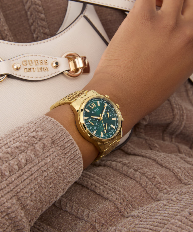 Gold GUESS Ladies Gold Tone Multi-function Watch with a blue face on a wrist, with a blurred background