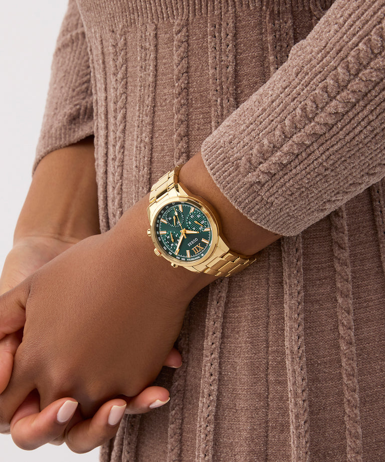 Gold GUESS Ladies Gold Tone Multi-function Watch with a green face on a wrist wearing a brown sweater.