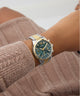Close-up of a person wearing a Guess GUESS Ladies 2-Tone Multi-function Watch on a neutral background