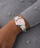GUESS Ladies Silver Tone Date Watch with a pink face on a wrist against a gray textured background