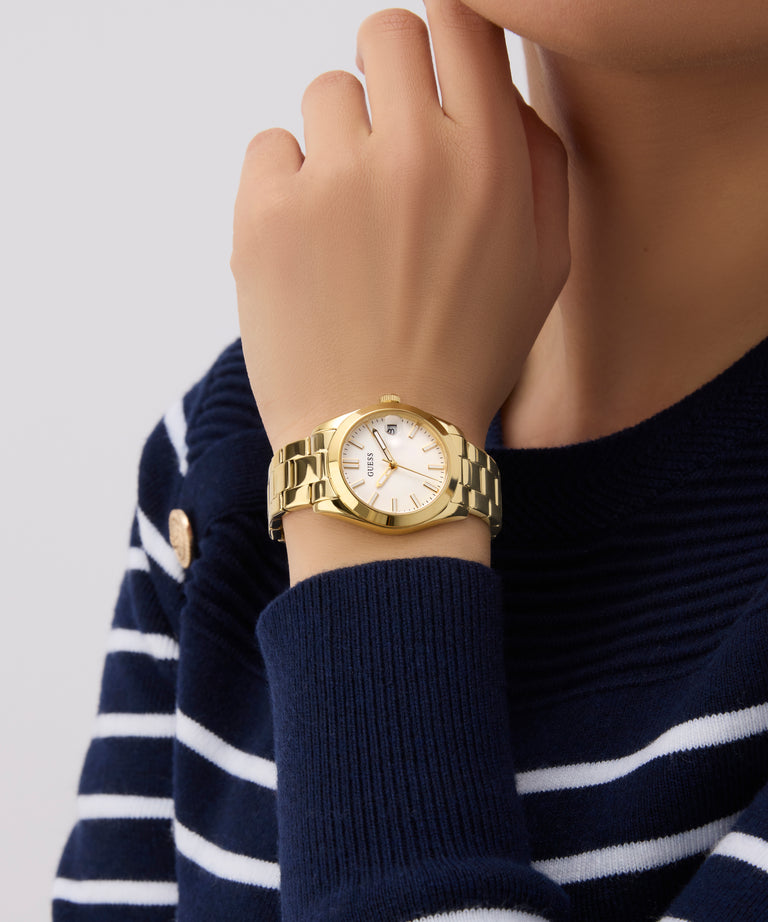 Gold GUESS Ladies Gold Tone Date Watch on a person wearing a navy sweater with white stripes.