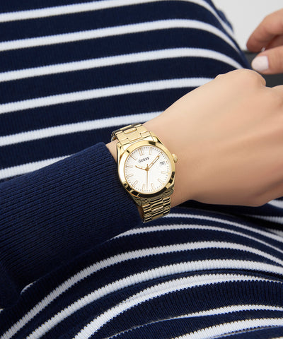 Gold GUESS Ladies Gold Tone Date Watch on a wrist with a person wearing a navy and white striped shirt