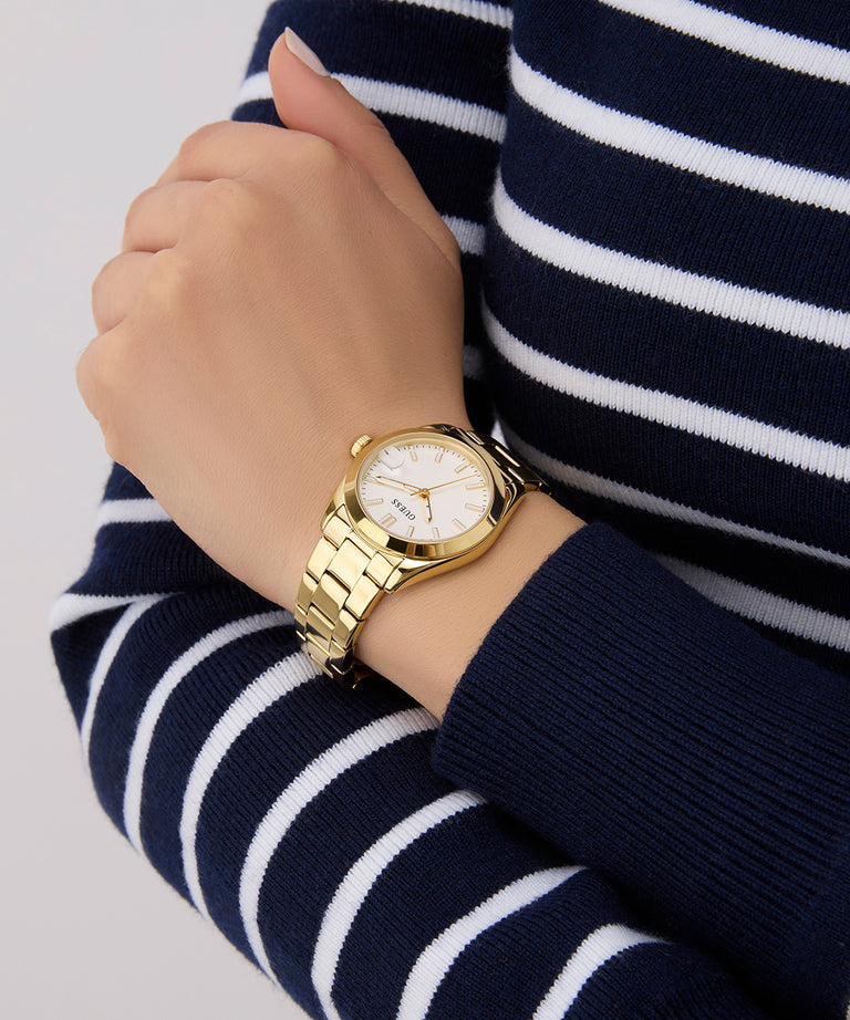 Gold GUESS Ladies Gold Tone Date Watch on a wrist with a navy and white striped sweater