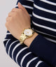 Gold GUESS Ladies Gold Tone Date Watch on a wrist with a navy and white striped sweater