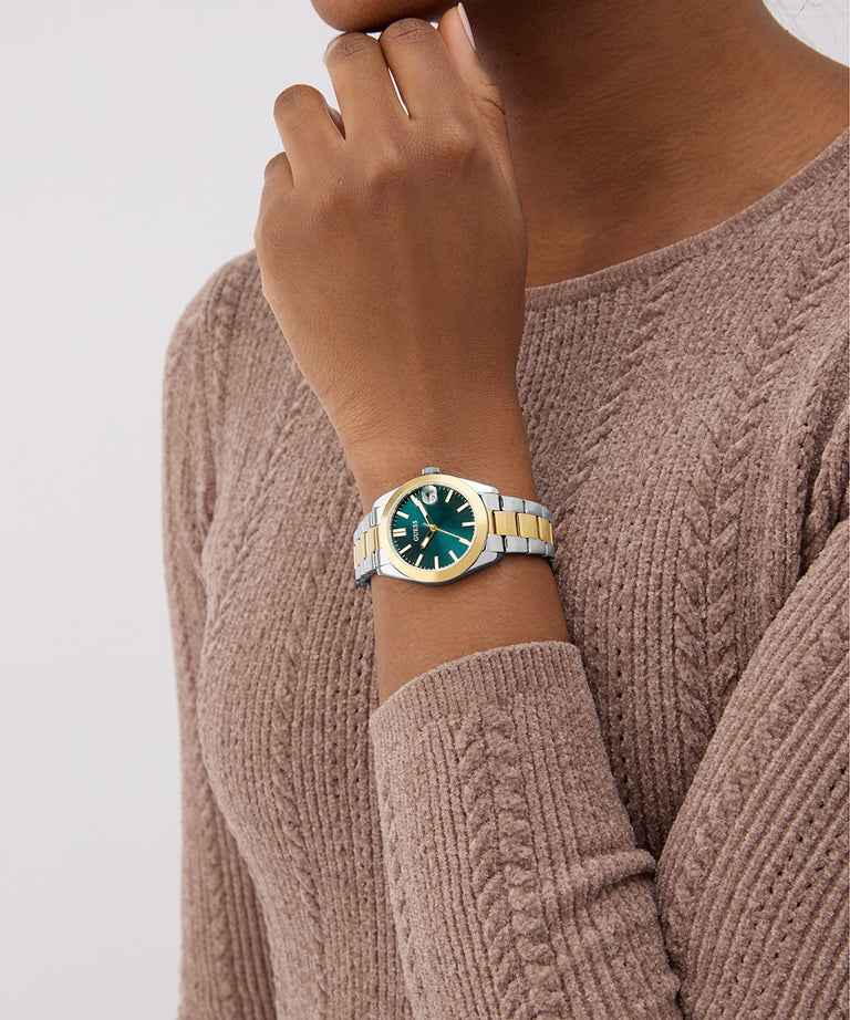 Person wearing a gold and green watch on a plain background