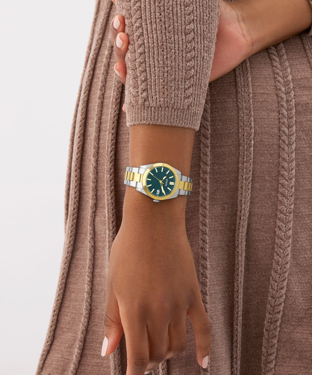 Hand wearing a gold and blue watch with a neutral background