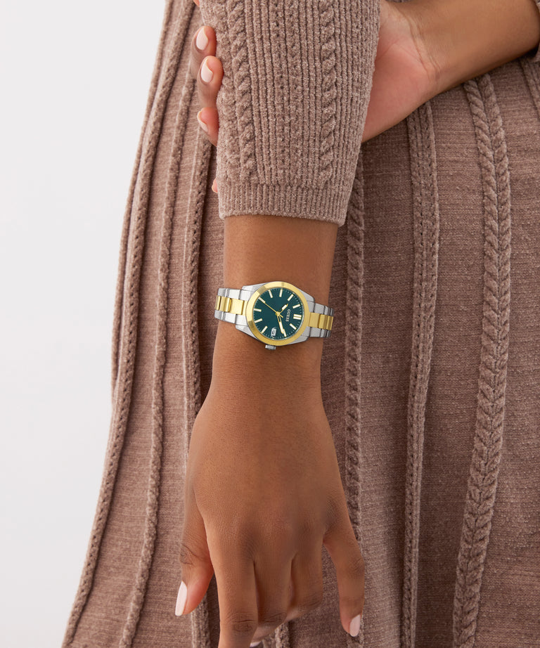 Hand wearing a gold and blue watch with a neutral background